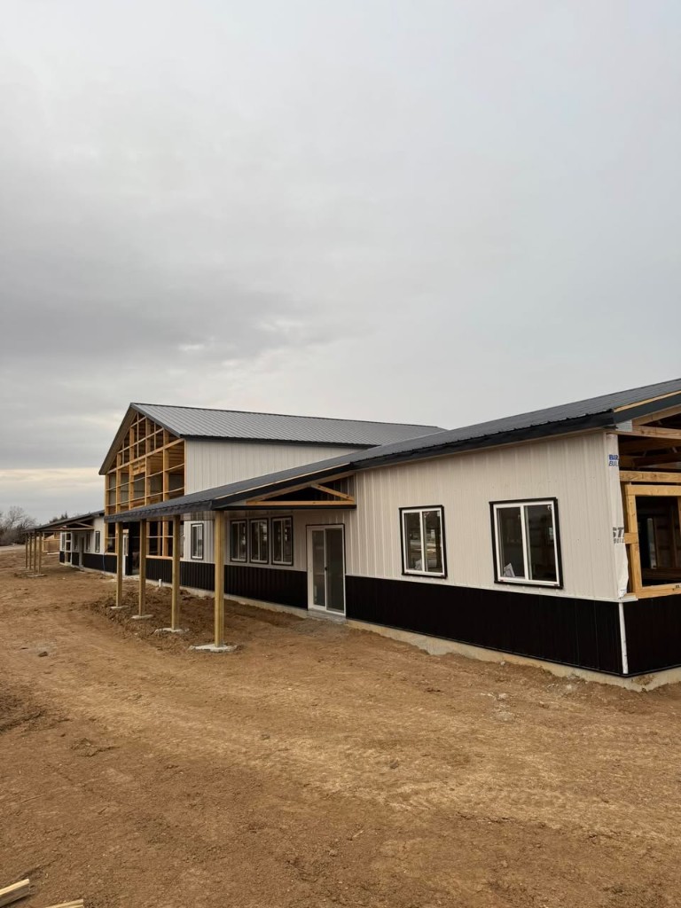Full-length facade on an overcast day: white upper walls, black wainscot, and lean-to porch roof.