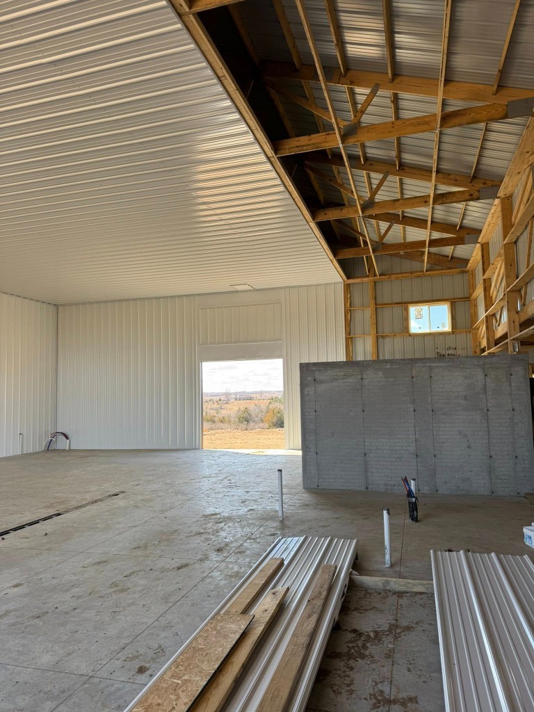 Shop bay with white liner on one side, exposed framing on the other, partition wall, and floor rough-ins.