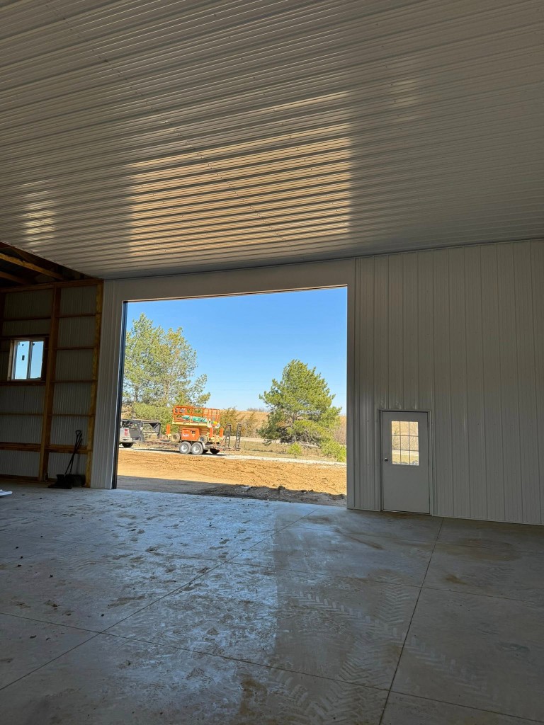 Interior toward open overhead frame: white ceiling liner, walk door, and equipment visible outside.