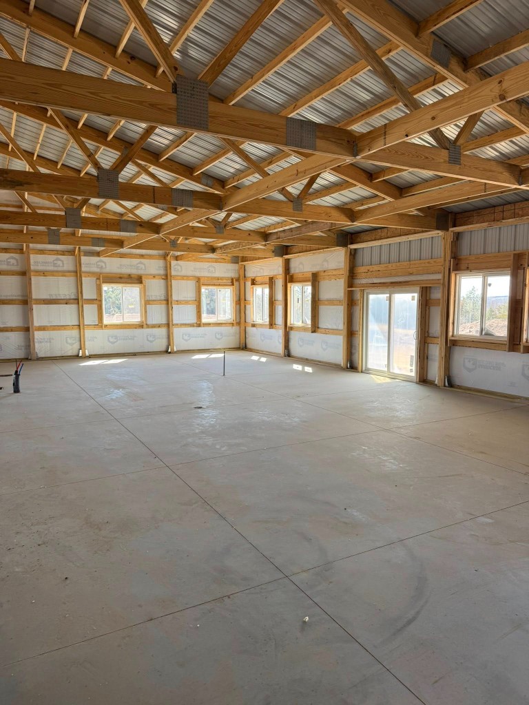 Open shell with house wrap, sliding windows, patio door, and exposed trusses to the metal roof deck.