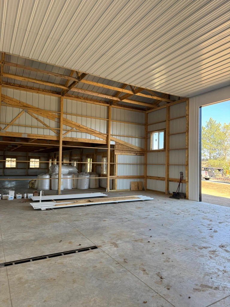 High-clearance shop space with white metal liner toward the living partition and open overhead door.