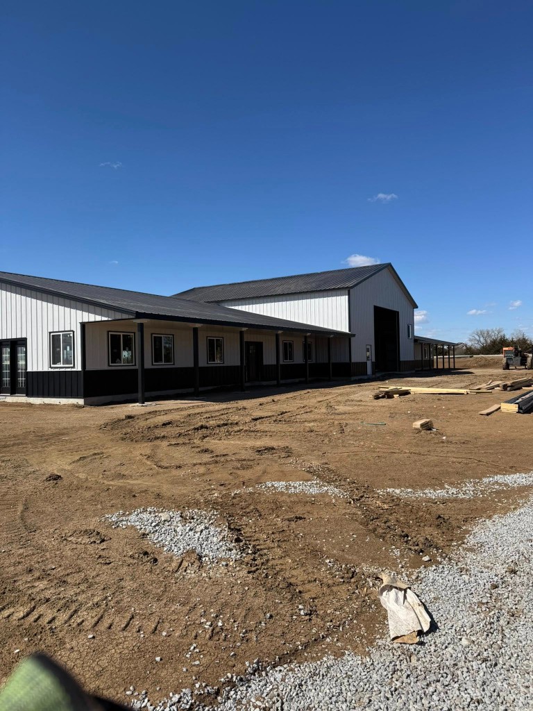 Porch run with black posts, glass doors, and a tall shop bay opening at the rear under bright sky.