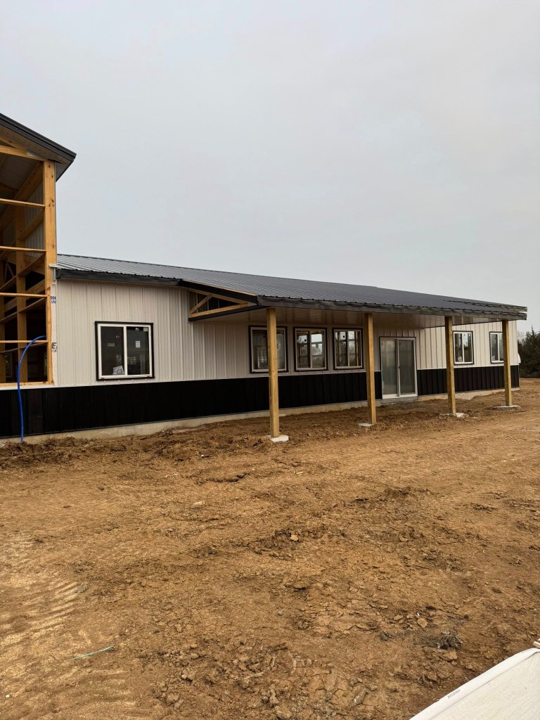 Long elevation with wood porch posts, white-trimmed windows, sliding door, and an open framed bay at the far end.