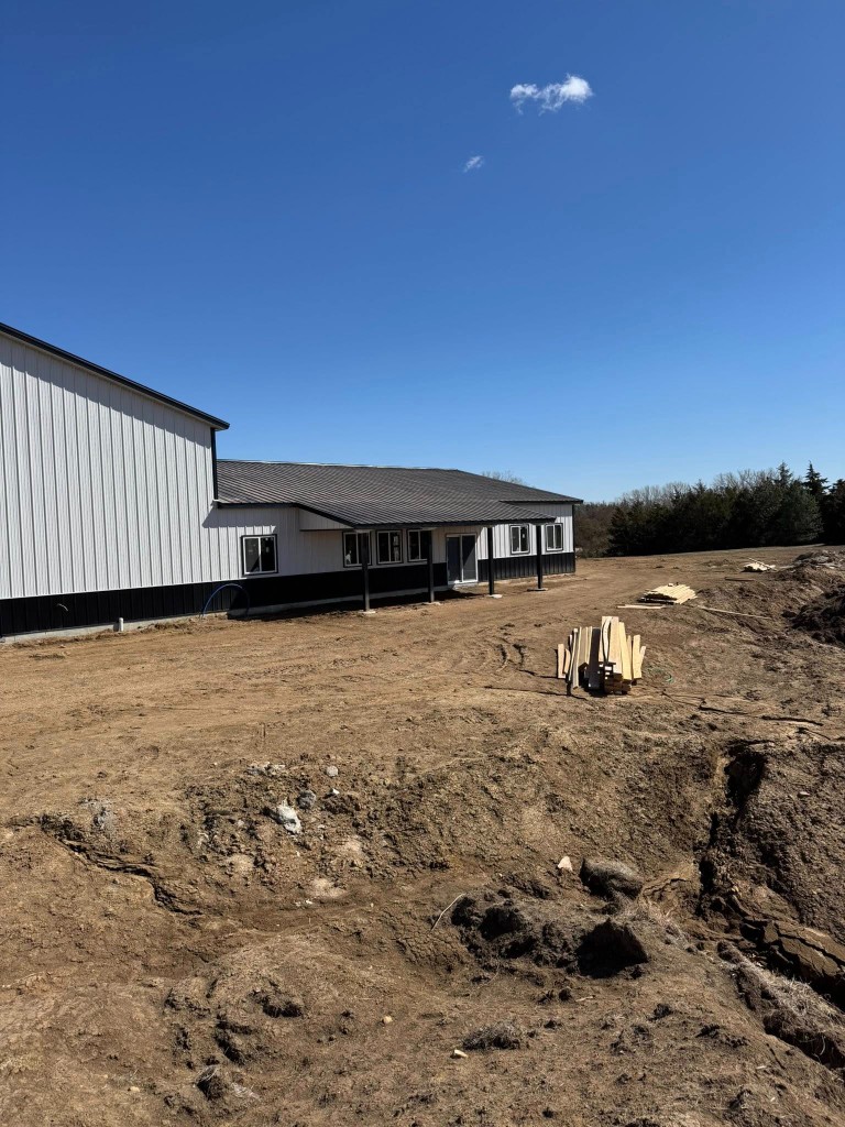 White and black metal shouse with deep porch, glass doors, and tall shop bay under a clear blue sky.