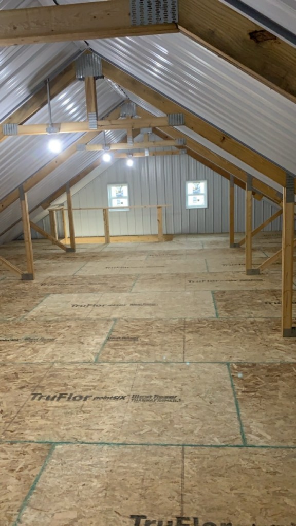 Loft gable end with paired windows, white metal walls, and stair opening.
