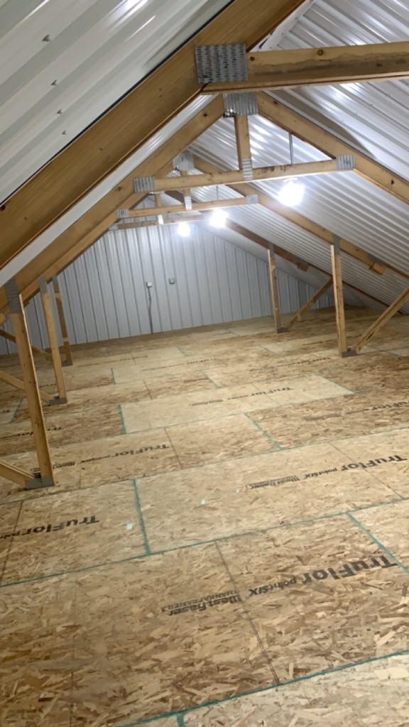 Loft with white metal liner, exposed trusses, and OSB subfloor under construction.