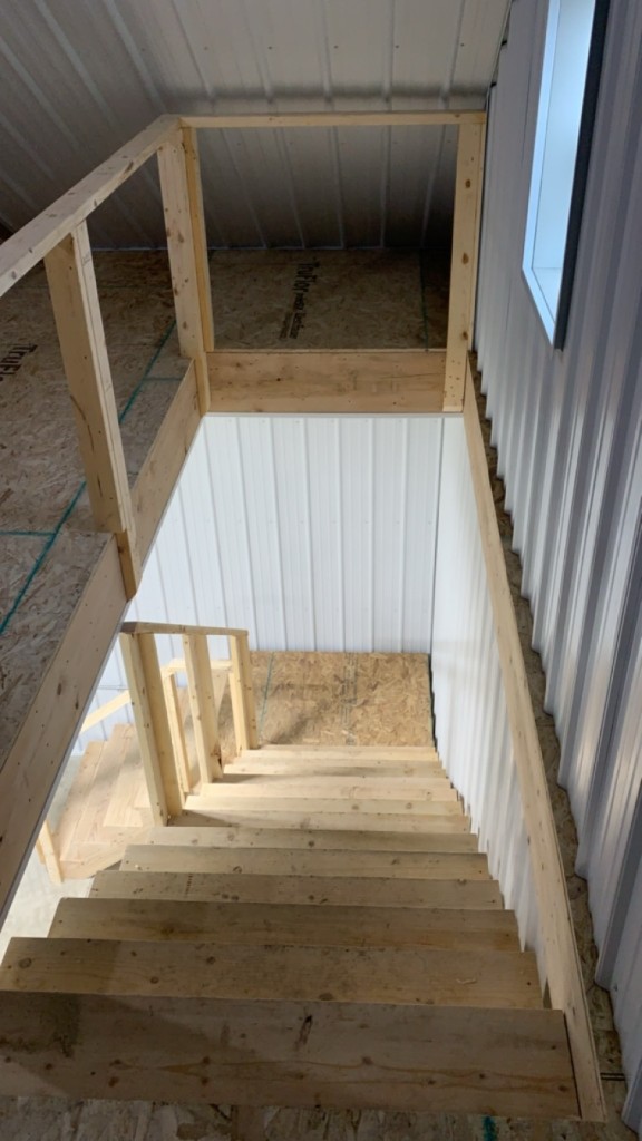 Stair run from loft: white metal walls, wood treads, and rough guard framing.