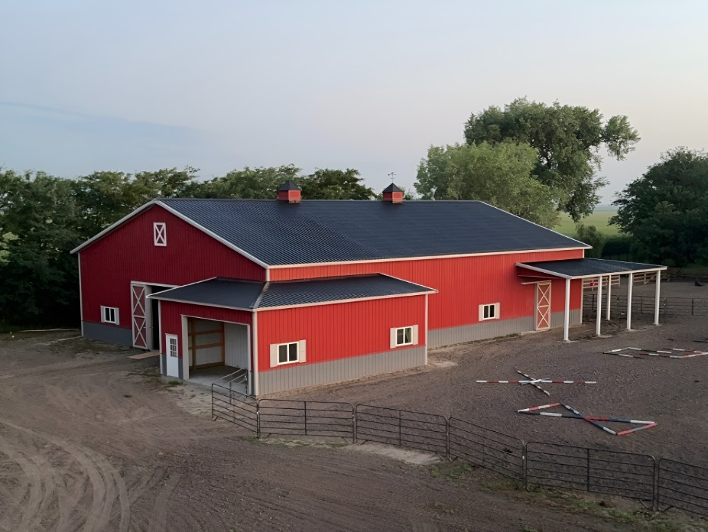 Red equestrian barn with cupolas and covered porch—post-frame horse barn in Nebraska.