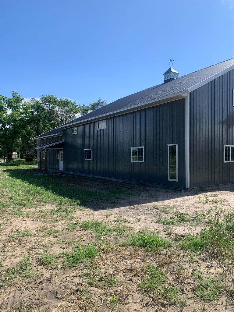 Charcoal metal barndominium-style post-frame building with white trim and dual ridge cupolas on a rural lot near Superior, Nebraska.