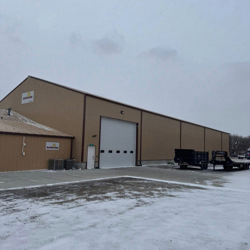 Large tan metal commercial building with white overhead door, walk door, dark trim, and winter site—industrial or fleet-scale shell.