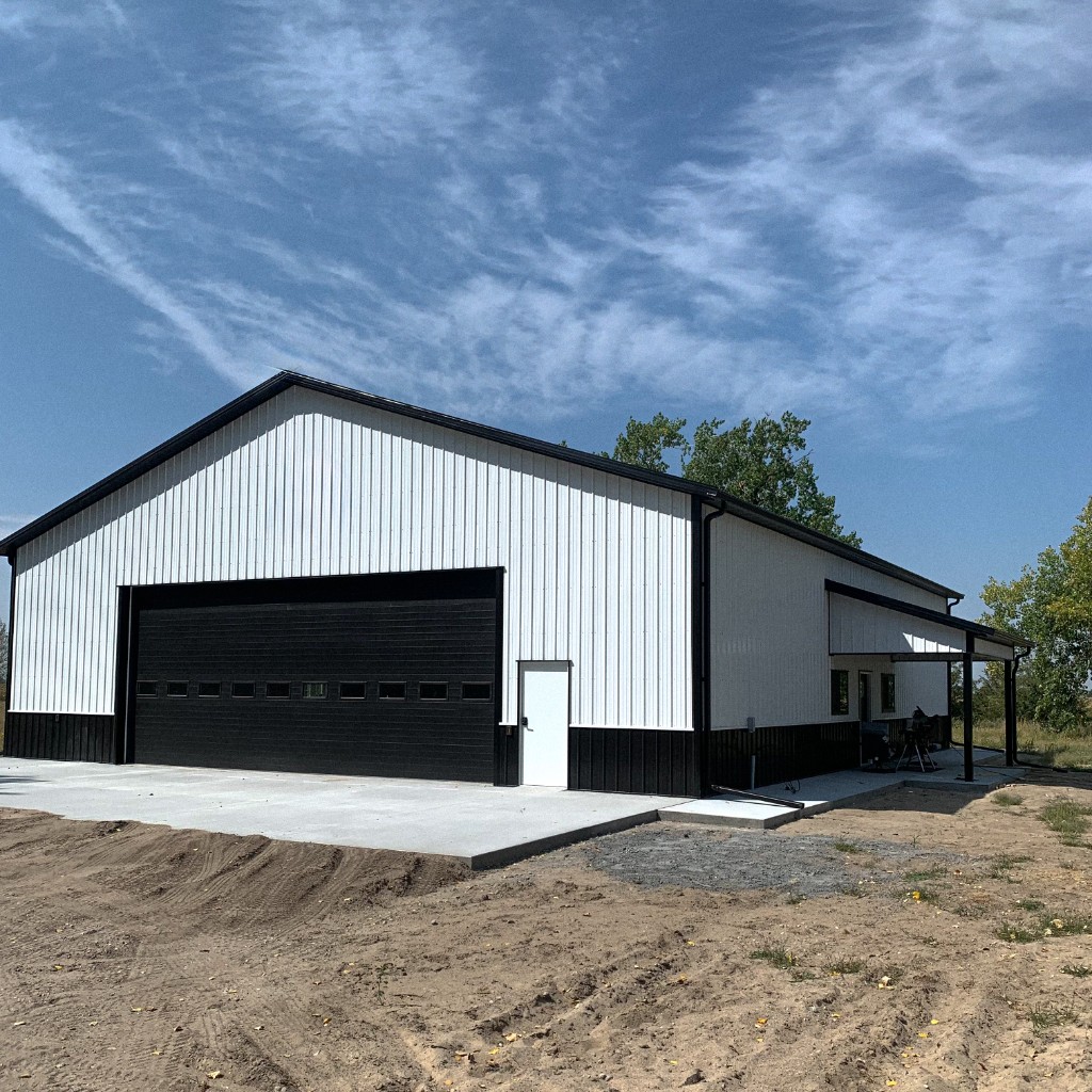 White and black two-tone post-frame hobby shop in Wood River, Nebraska—overhead door, walk door, and side porch on a barndominium-style shell.