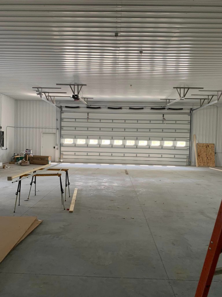 Interior toward large white sectional overhead door with windows, walk door, conduit, and work in progress on the floor.