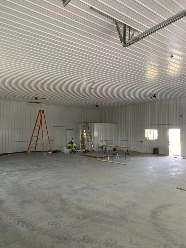 Gable end and side entry: black roof and trim, white vertical siding, concrete walk, and walk door with window.